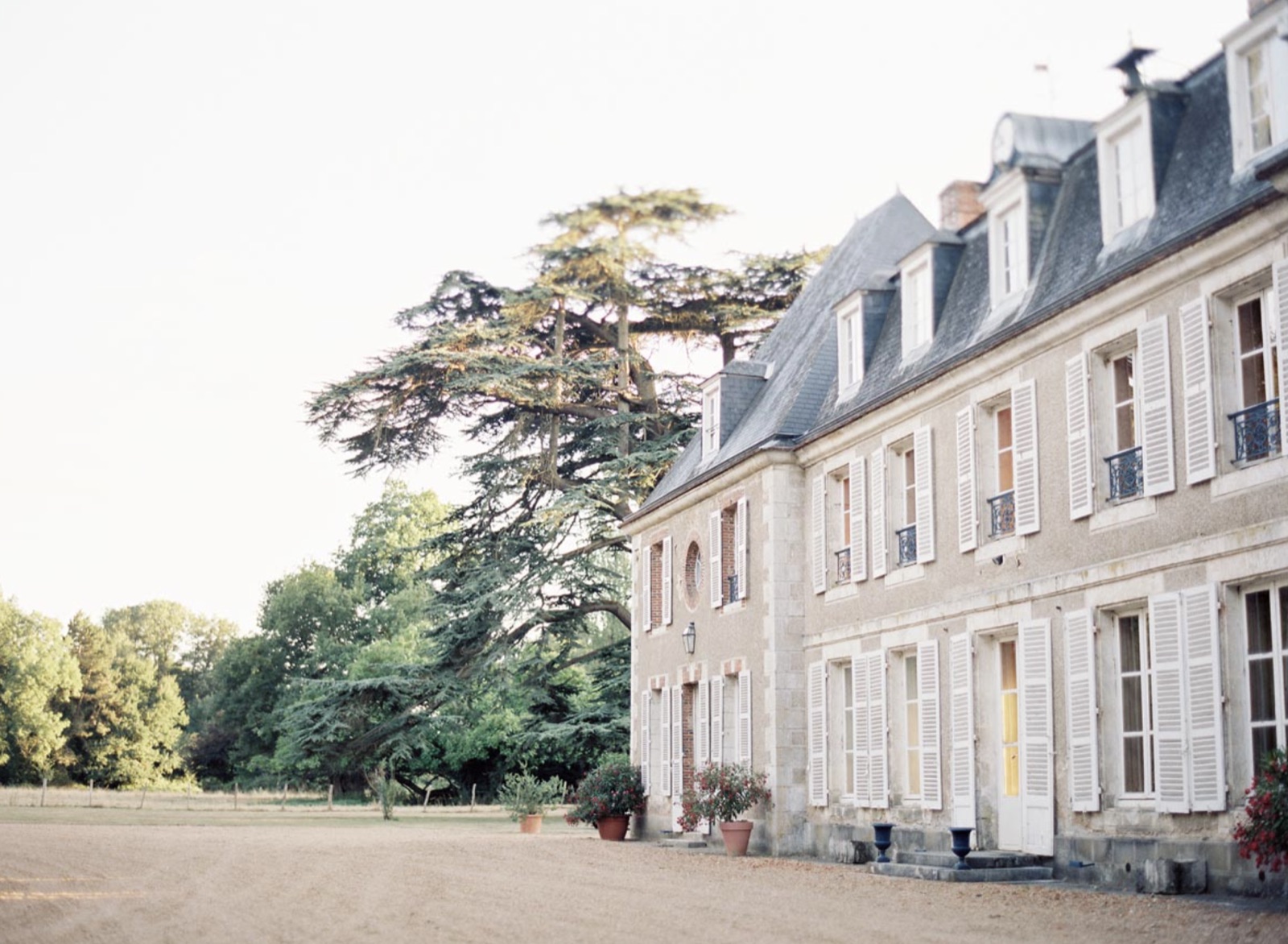The front of the château at golden hour, shutters open above the gravel courtyard
