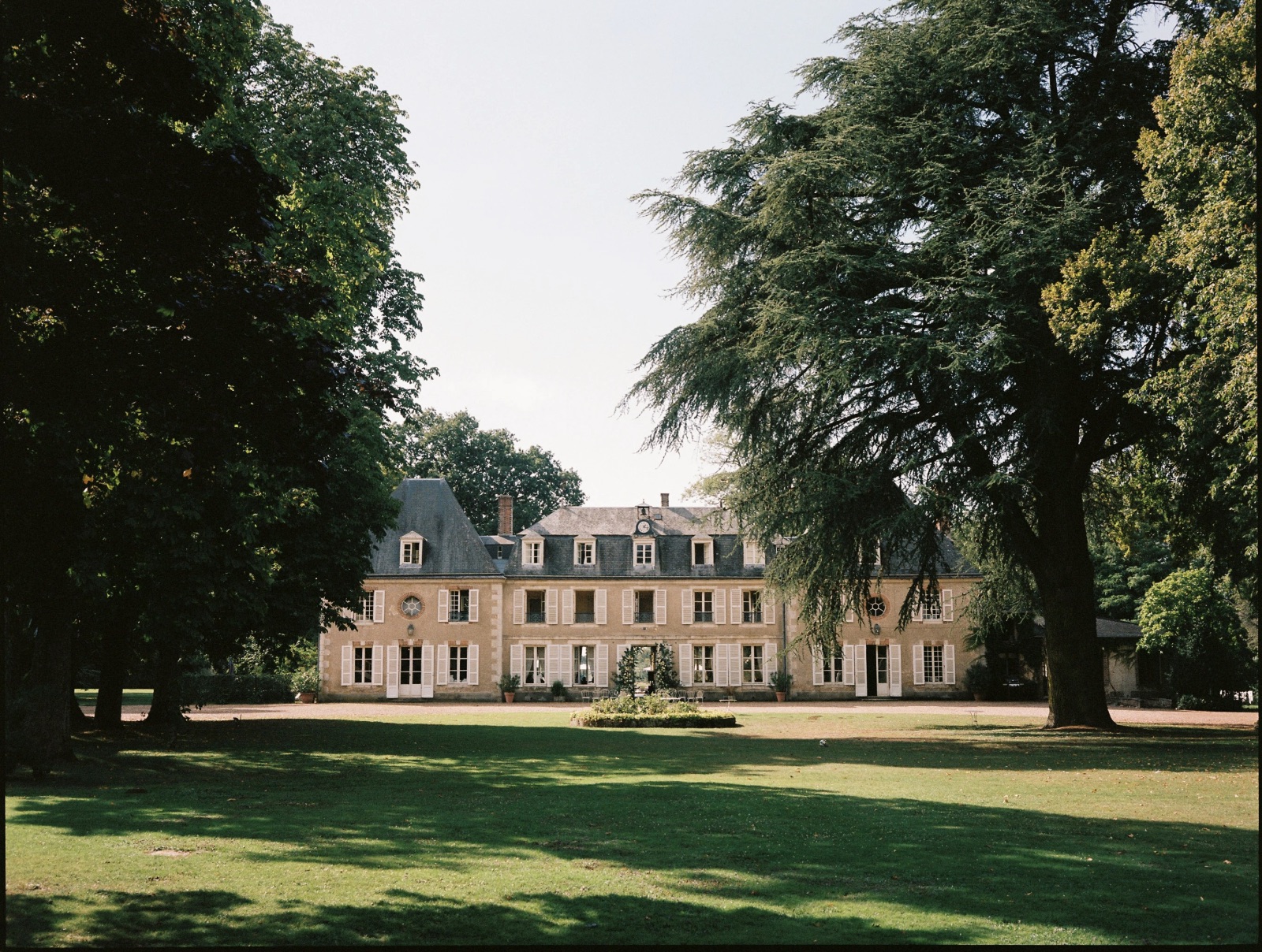 The château seen across the wide lawn, framed by old cedar trees
