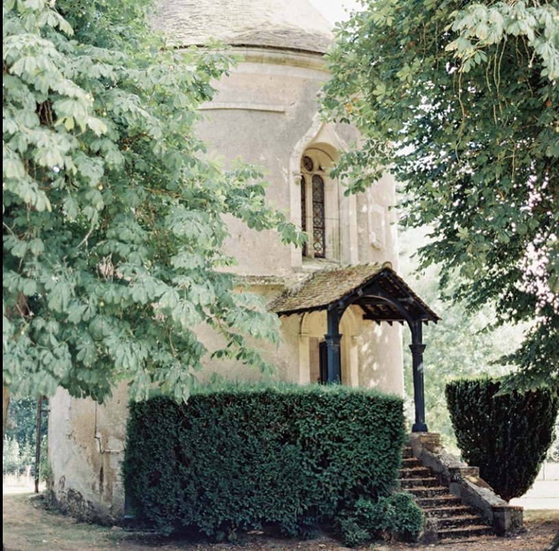 A stone turret with a covered porch and steps, half hidden behind hedges